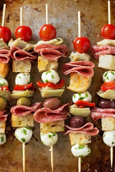 an assortment of appetizers on skewers with tomatoes, olives and meat