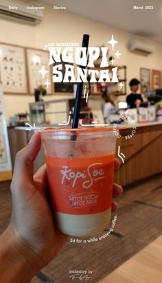 a person holding up a drink in front of a counter with the words topi santa on it