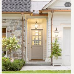 the front door of a house with two lights on and flowers in pots next to it