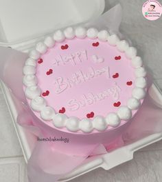 a pink birthday cake with white frosting and red hearts on the top in a box