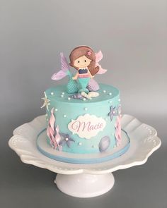 a blue cake with a little mermaid sitting on it's top and under the word mate