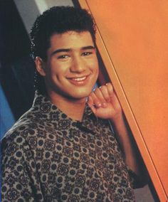 a young man is smiling and leaning against an orange wall with his hand on his chin