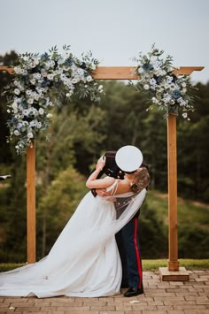 a bride and groom kissing under an arch decorated with blue flowers at the end of their wedding day