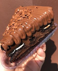 a hand holding a piece of cake with chocolate frosting