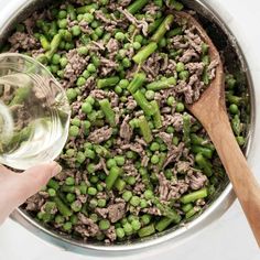 a person is pouring water into a pot filled with meat and asparagus on the side