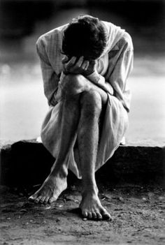 a black and white photo of a man sitting on the ground with his head in his hands