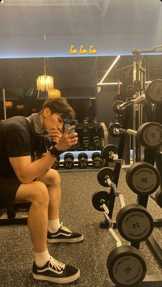 a man squatting down in front of a row of dumbbells and looking at his cell phone