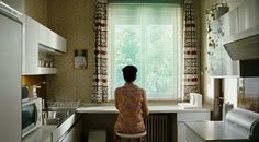 a woman is standing at the window in her kitchen looking out to the yard outside