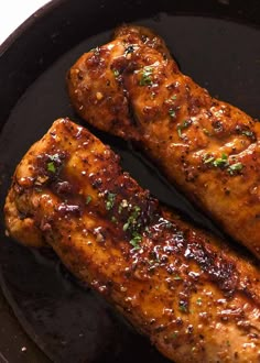 two pieces of chicken in a pan with sauce and herbs on top, ready to be cooked