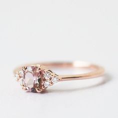 a pink diamond ring with three diamonds on the band and an oval shaped center stone