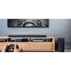 a person holding a game controller in front of a flat screen tv on a wooden entertainment center