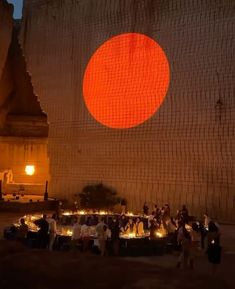 people standing around in front of a building with a large orange circle on the wall