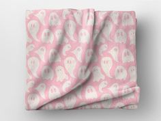 a pink and white blanket with ghost faces on it's side, in front of a gray background