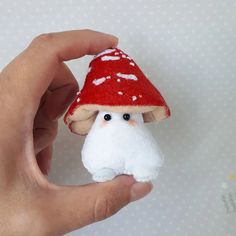 a hand holding a small red and white mushroom