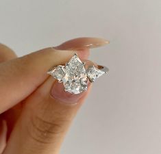 a woman's hand holding an engagement ring with three pear shaped diamonds on it