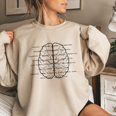 a woman sitting on a bed wearing a sweatshirt with the words brain printed on it