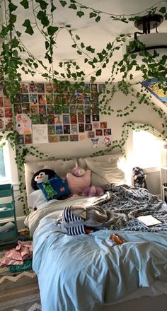 an unmade bed with plants growing on the wall above it and pictures hanging from the ceiling