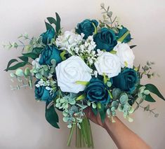 a bouquet of white and blue flowers is being held by a person's hand