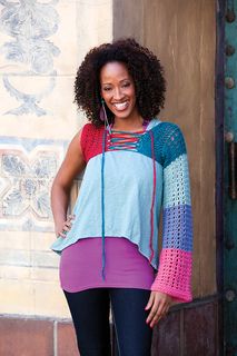 a woman with an afro standing in front of a wall wearing a multicolored top