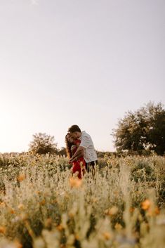 a man and woman hugging in the middle of a field with orange flowers on it