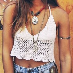 a woman wearing a white crochet top and denim shorts standing in front of a wall