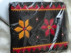 a black bag with red and yellow flowers on it sitting on a white cloth covered surface