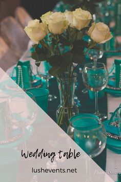 the table is set with white roses and teal place settings