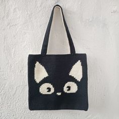 a crocheted black and white cat bag hanging on a wall with eyes drawn on it