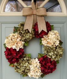 a wreath with red and white flowers is hanging on the front door to welcome guests