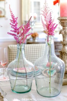 two vases with flowers in them sitting on a table next to a candle holder