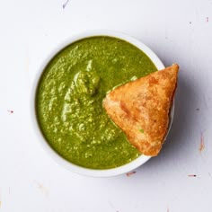 a white bowl filled with green sauce and a piece of bread