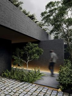 a man walking down a sidewalk next to a black building with trees and plants on it