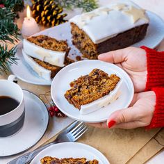 someone holding two plates with slices of cake on them next to a cup of coffee