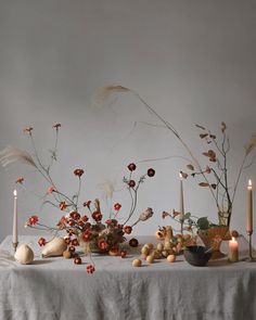 an arrangement of flowers and candles on a table with a white linen draped over it