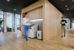 an office with hard wood floors and lots of windows on the wall, along with a printer machine