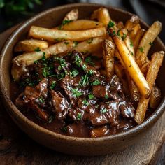 a bowl filled with meat and fries on top of a wooden table