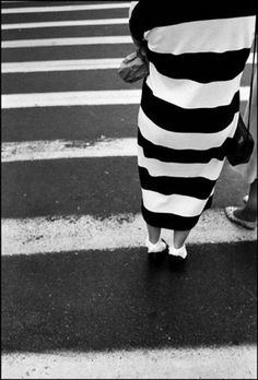 black and white photograph of people walking across the street in striped dress on crosswalk