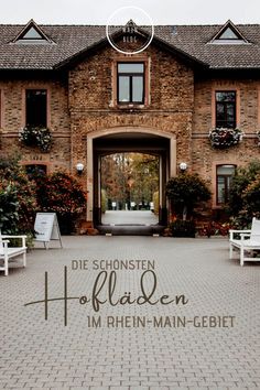 the front entrance to a large brick building with white chairs and flowers in pots on either side