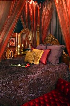 a bed with lots of pillows and blankets on it's headboard, surrounded by red drapes