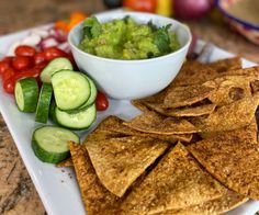 a white plate topped with tortilla chips and cucumber next to a bowl of guacamole