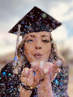 a woman wearing a graduation cap and gown blowing bubbles in front of her face while she holds