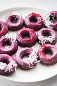 purple donuts with white sprinkles and shredded coconut on a white plate