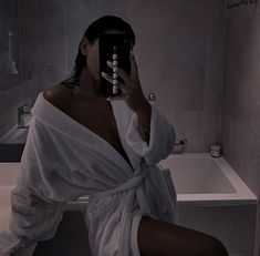 a woman in a bathrobe taking a selfie with her cell phone while sitting on a toilet