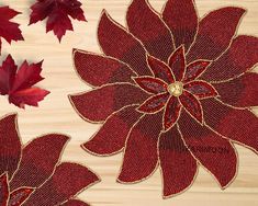 red flowers and leaves on a wooden surface with some gold bead work in the middle