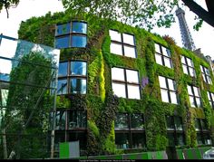 an office building covered in green plants on the side of it's face and surrounded by trees