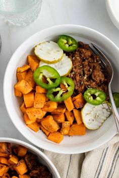 two bowls filled with food sitting on top of a white tablecloth next to silverware