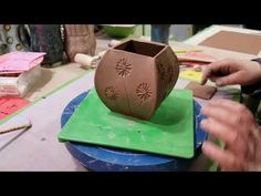 a person is making a vase out of clay on a green surface with other crafting supplies in the background