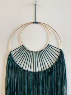 a green wall hanging with two circular rings and fringes on the top of it