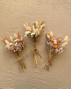 three dried flowers sitting on top of a white cloth covered table next to each other