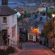 an empty street with some buildings on both sides and the ocean in the background at dusk